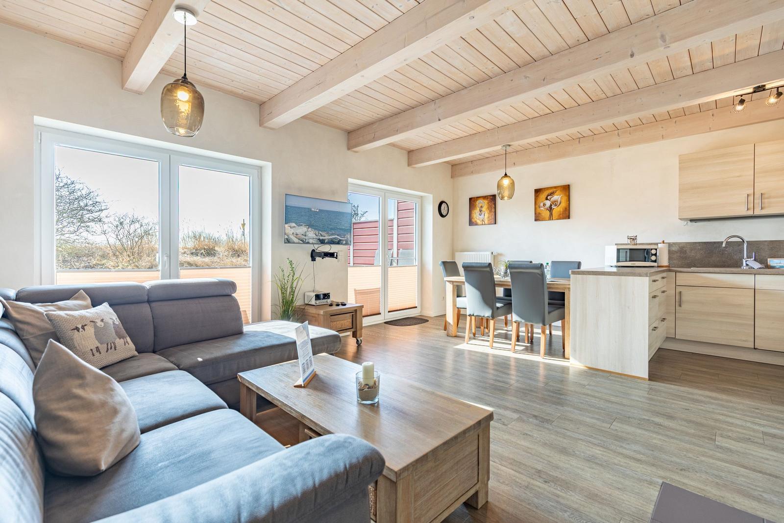 Wohnbereich mit Sofa, Essbereich und Küche unter Holzdecke.
