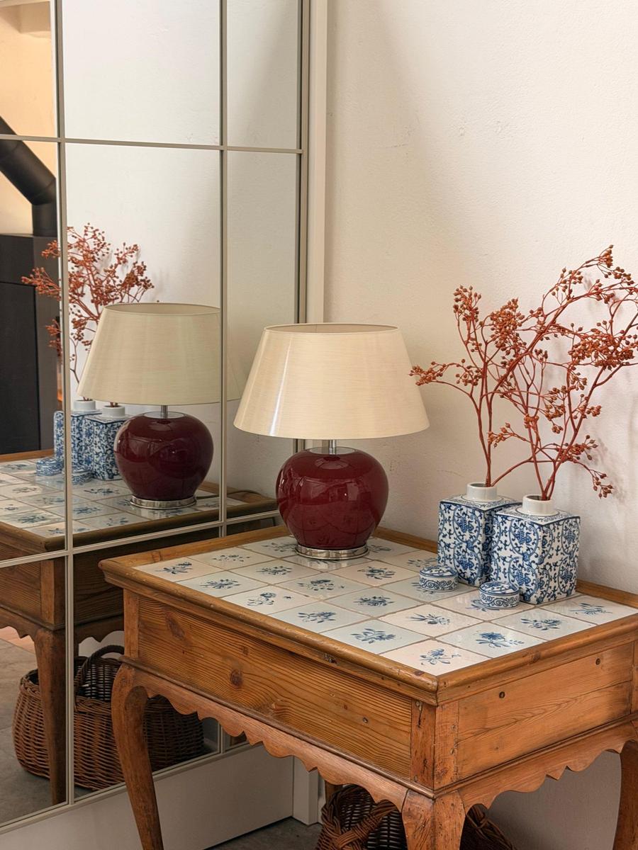 Holztisch mit blau-weißen Fliesen, roter Lampe und Vasen mit getrockneten Zweigen.