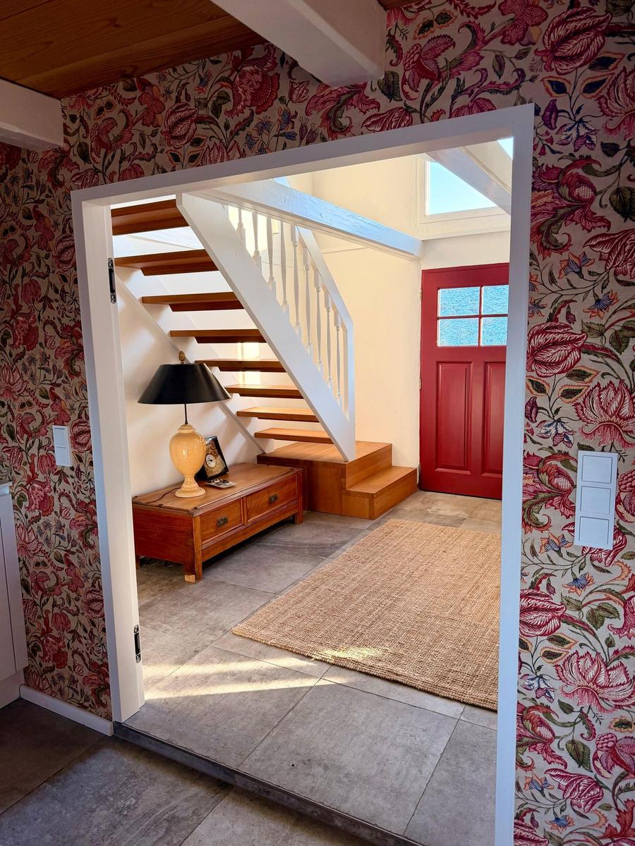 Hausgang mit Holztreppe, roter Tür und floraler Tapete.