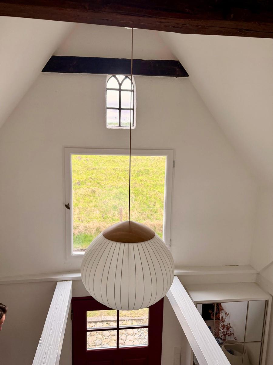 Hochwertige Pendelleuchte in einem Dachzimmer mit Fenster und Holzbalken.
