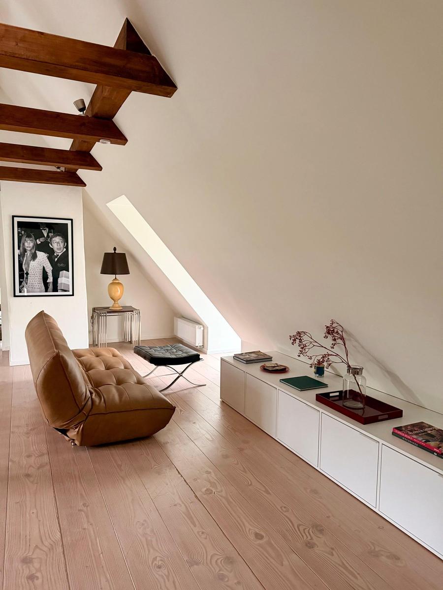 Wohnraum mit Holzboden, brauner Ledercouch und weißem Schrank unter schräger Decke.