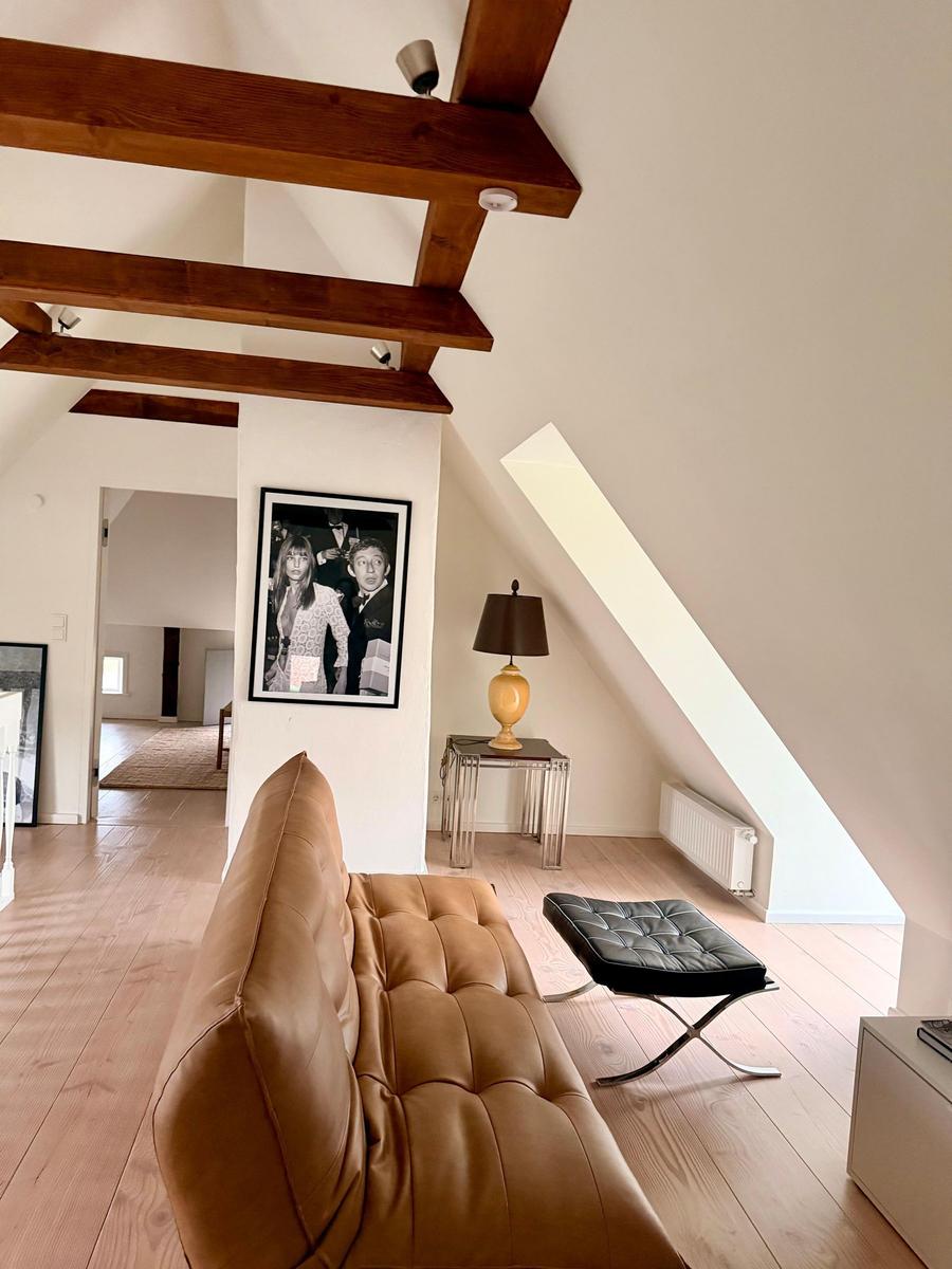 Wohnbereich mit braunem Ledersofa, Holzbalken und schräger Dachschräge.