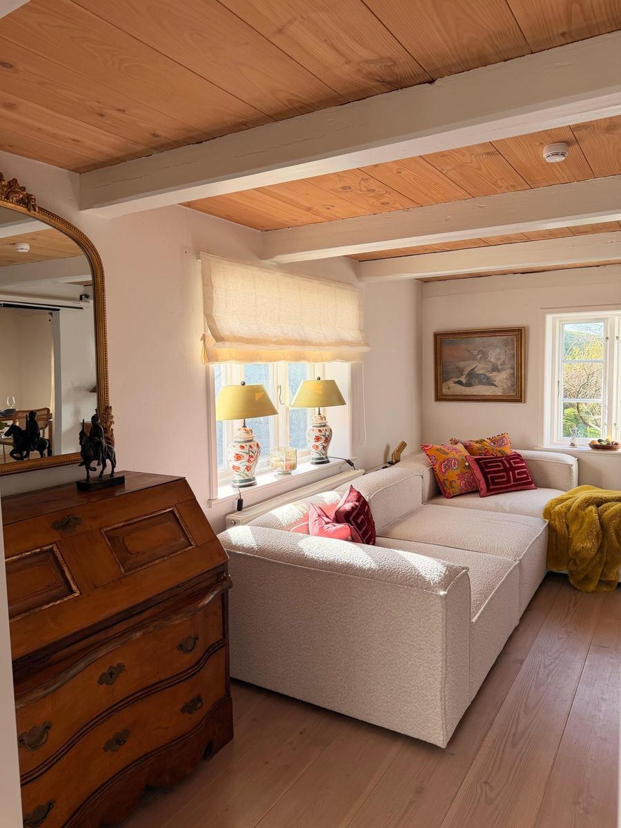 Wohnzimmer mit Sofa, Holzdecke und Fenster. Holzschrank und Lampen sind sichtbar.