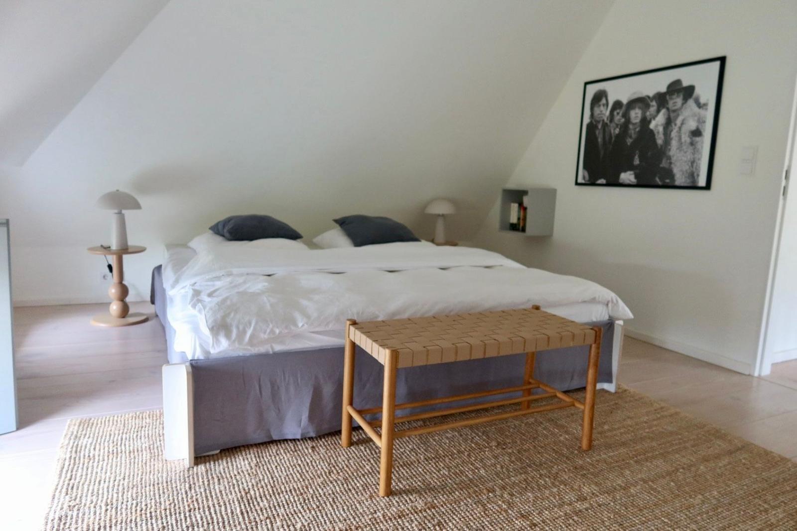 Schlafzimmer mit Doppelbett, Holzbank und Wandbild. Holzfußboden und Stehleuchten.