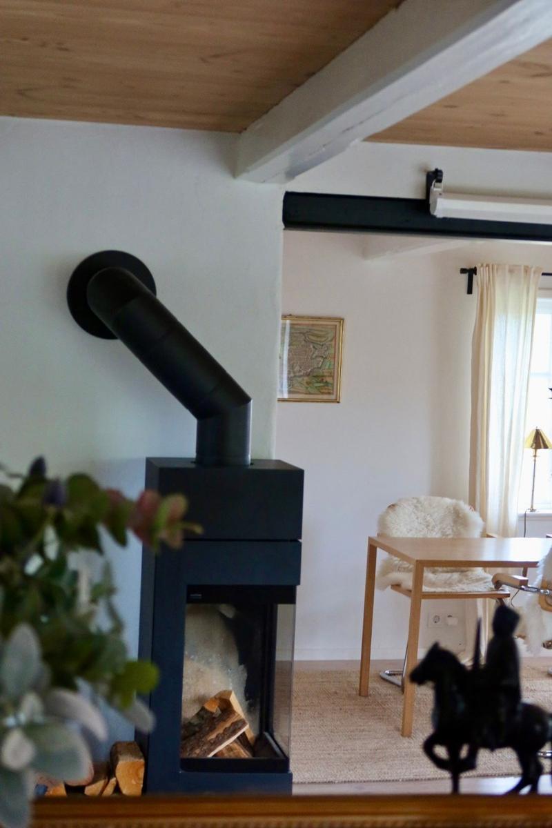 Schwarzer Kaminofen mit Holz im Vordergrund. Im Hintergrund Tisch und Stuhl mit Fellbesatz.