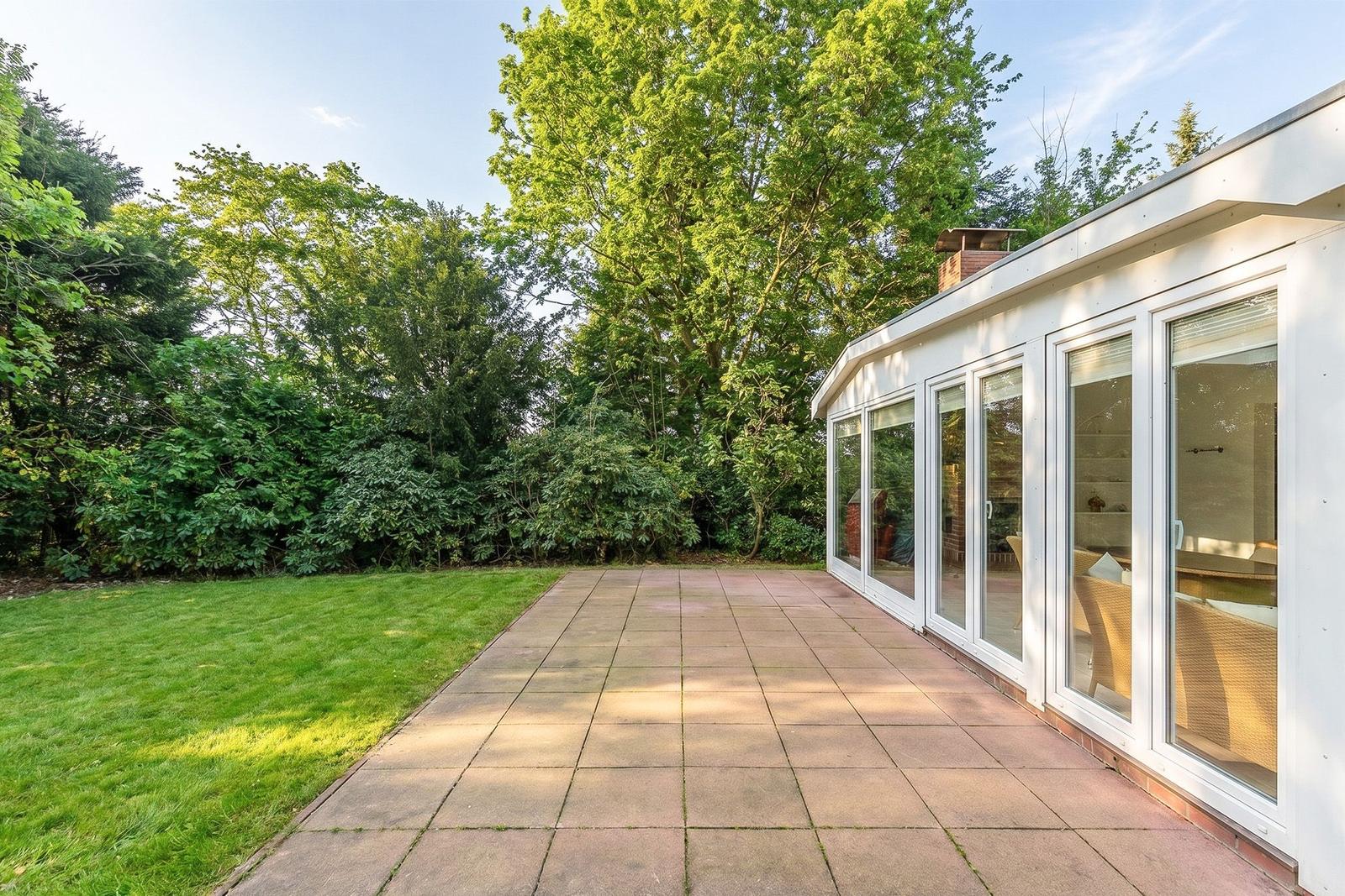 Terrasse mit Glasfront und grünem Garten hinter dem Haus.