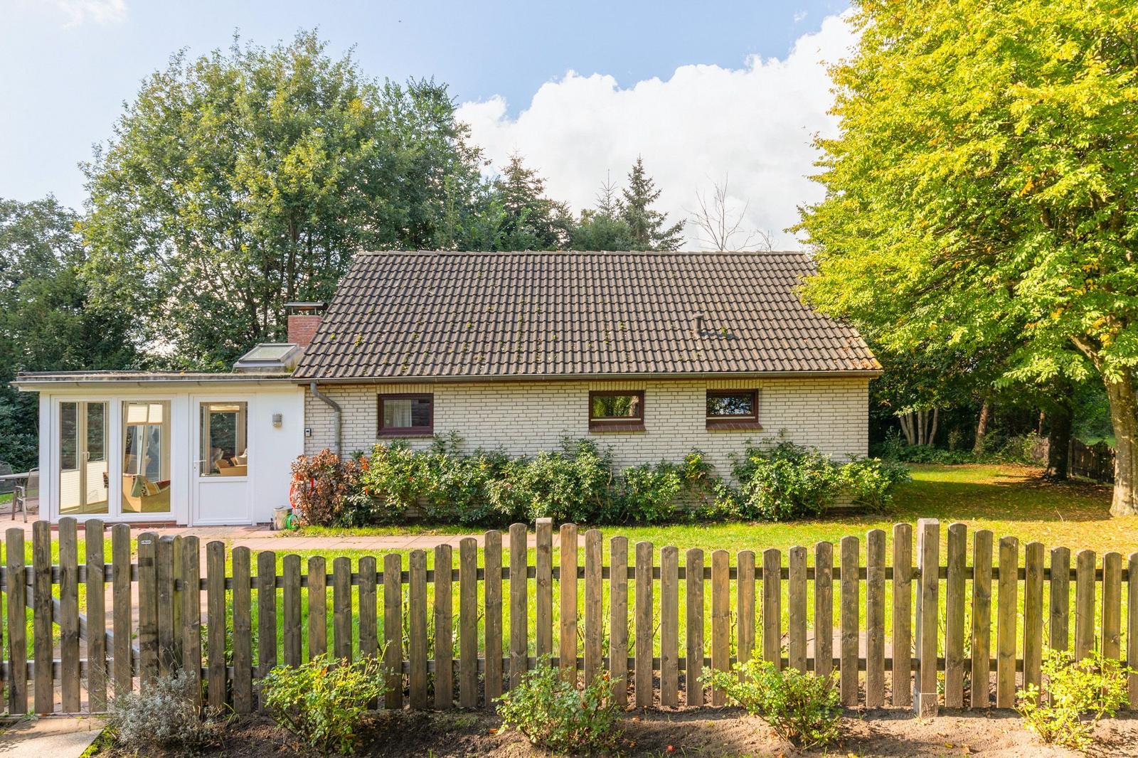 Ein Haus mit weißem Putz, Holzschindeldach und kleinem Garten hinter einem Holzzaun.