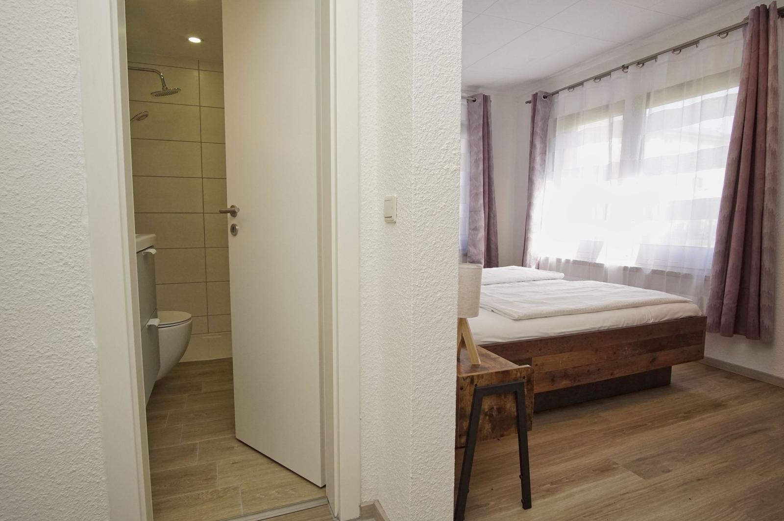 Schlafzimmer mit Holzbett und Dusche im Anschluss