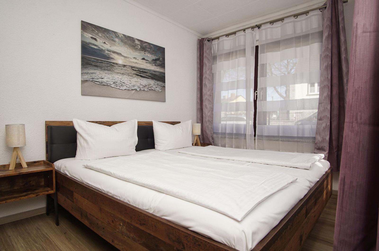 Ein Schlafzimmer mit Doppelbett, Wandbild und Fenster mit Vorhängen.