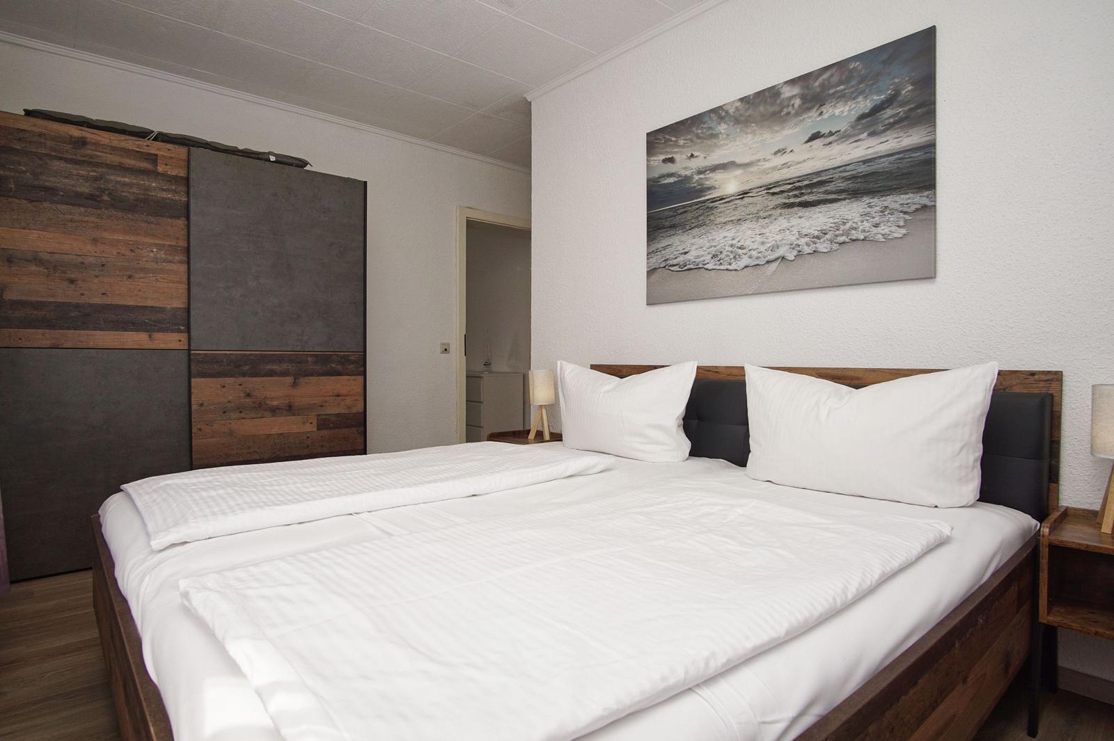 Schlafzimmer mit Doppelbett, Holzmöbel und Wandbild am Bett.