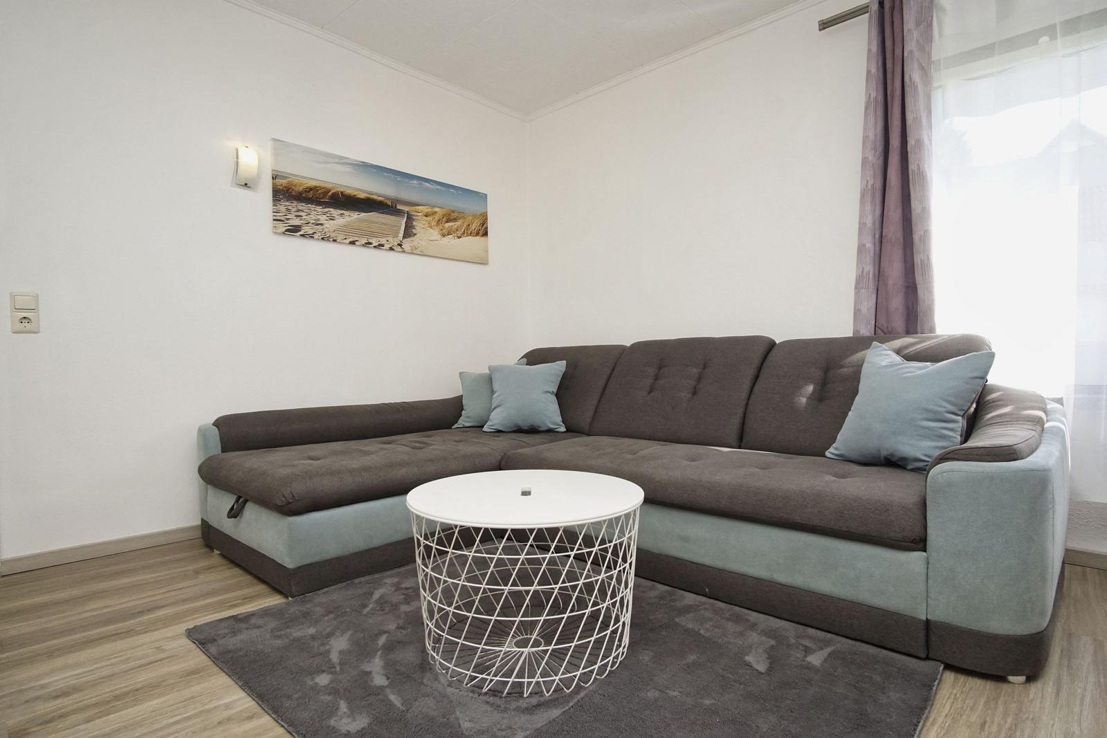 Wohnzimmer mit Ecksofa, runden Tisch und Wandbild.