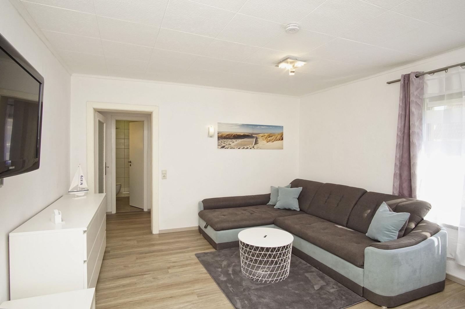 Wohnzimmer mit Ecksofa, runden Tisch und Fernseher an der Wand.