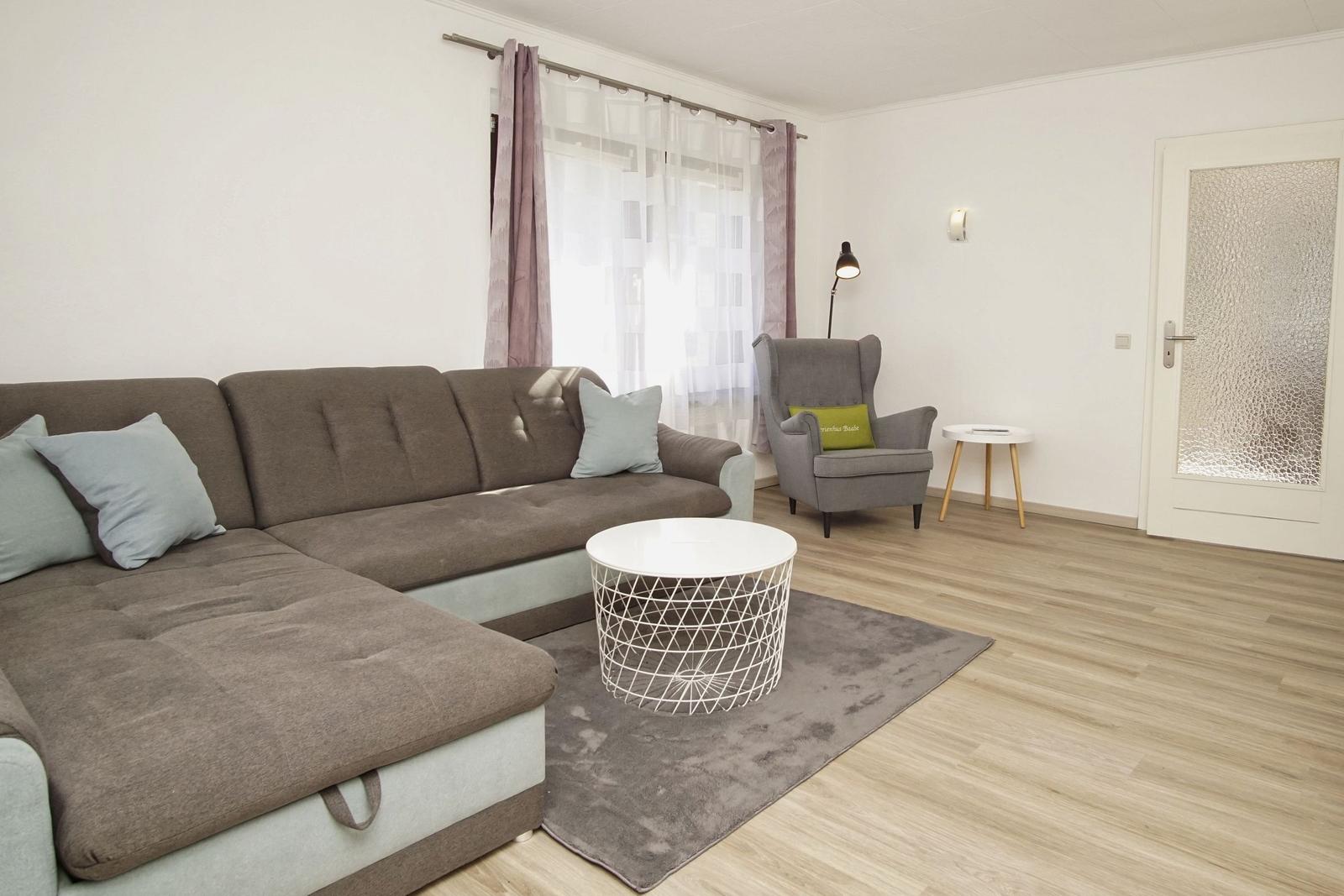 Wohnzimmer mit Sofa, Sessel, Tisch und Teppich auf Holzboden.