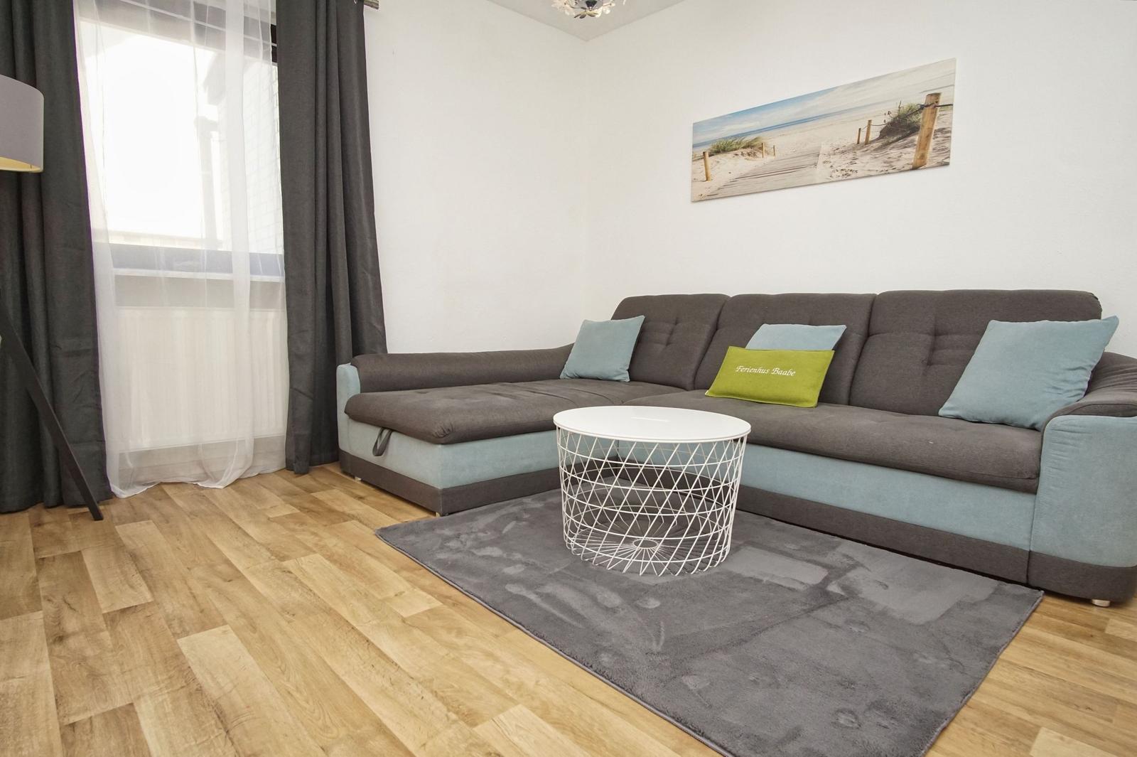 Wohnzimmer mit grauem Sofa, weißem Tisch und Holzboden.