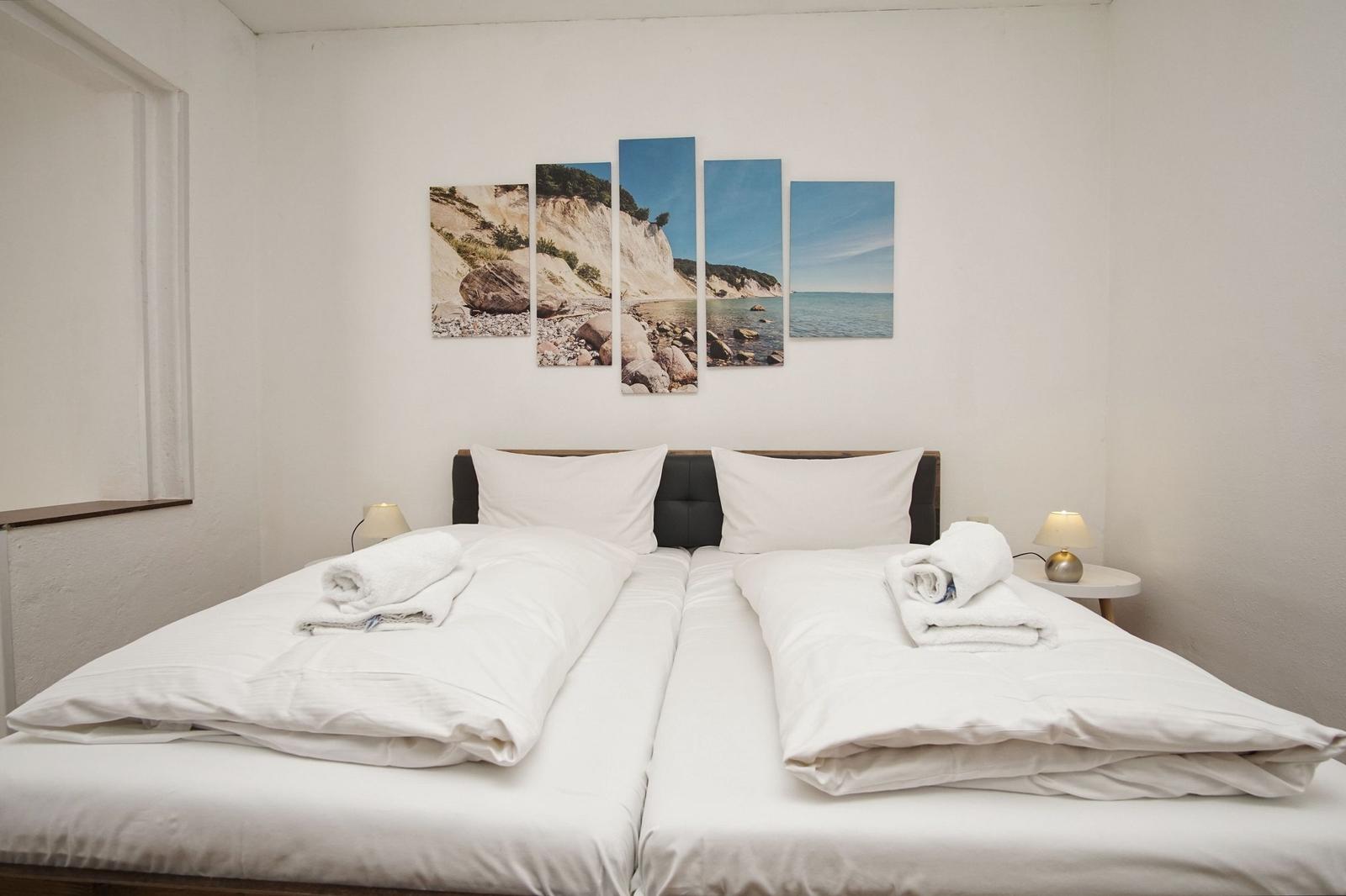 Zwei Betten mit weißen Bettwäsche und Handtüchern. Wandbild zeigt Küstenlandschaft.