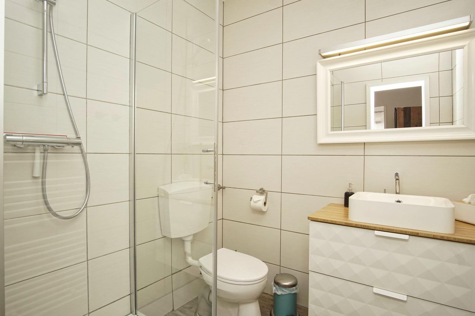 Bad mit Dusche, Toilette und Waschbecken mit Spiegel.