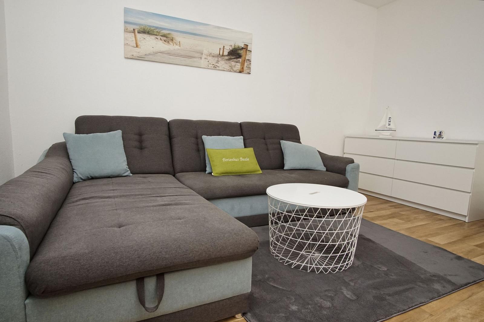 Ein Wohnzimmer mit grauem Sofa, runden Tisch und Wandbild.