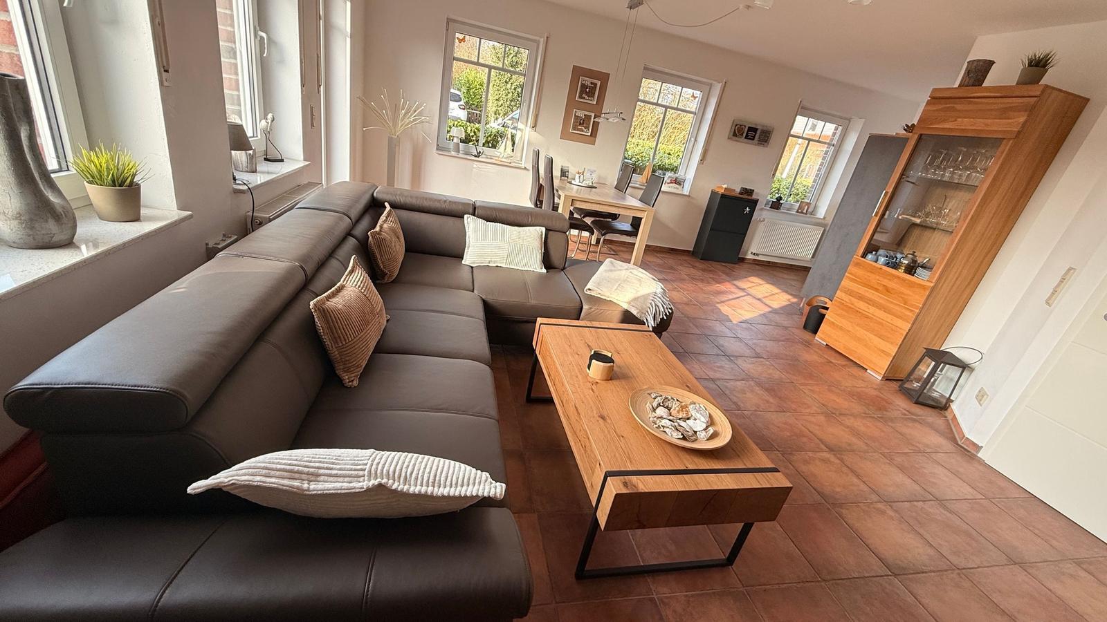 Wohnzimmer mit Ecksofa, Holztisch und Terrasse. Küche im Hintergrund.