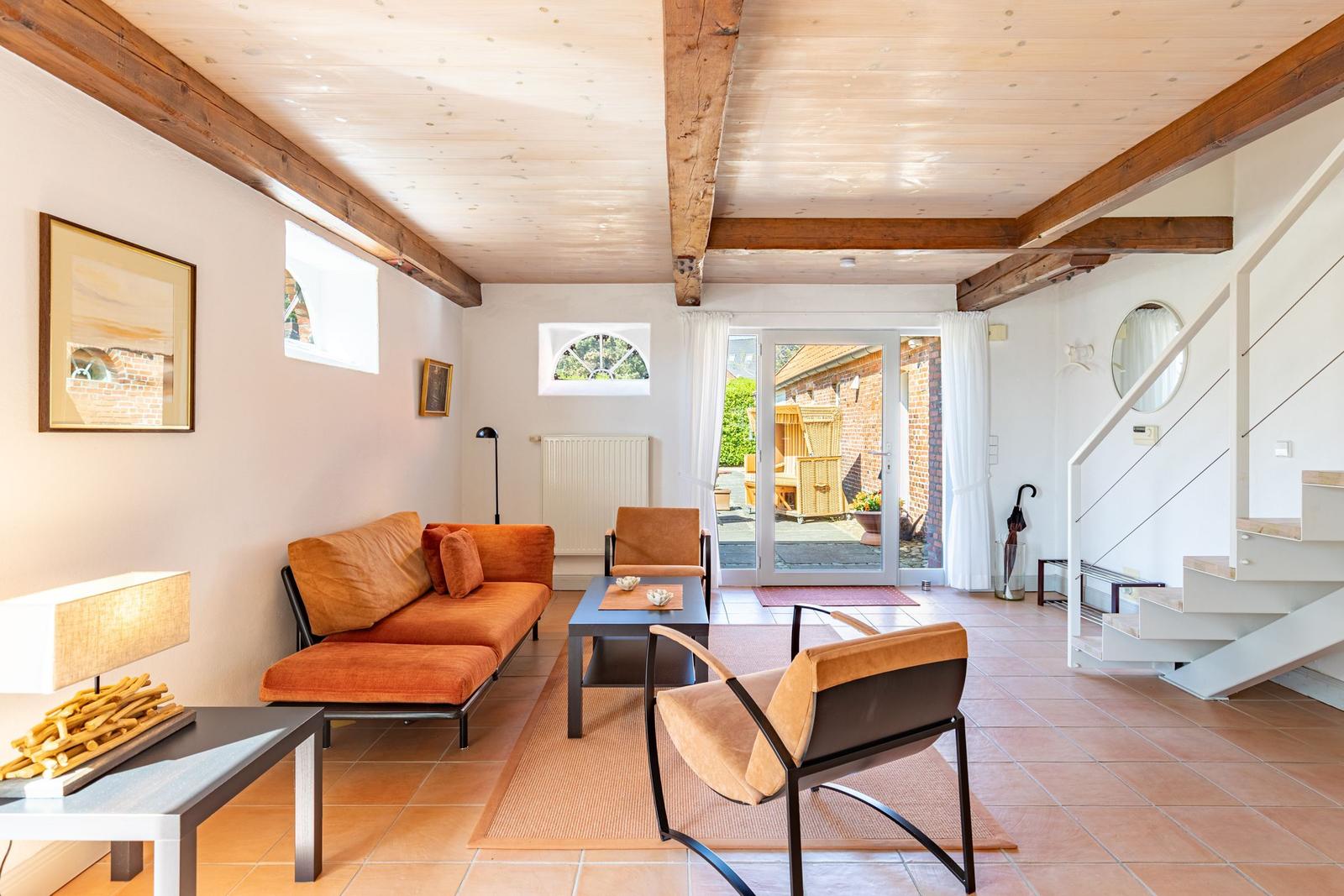 Wohnzimmer mit Holzbalken, orangefarbenem Sofa und Blick auf die Terrasse.