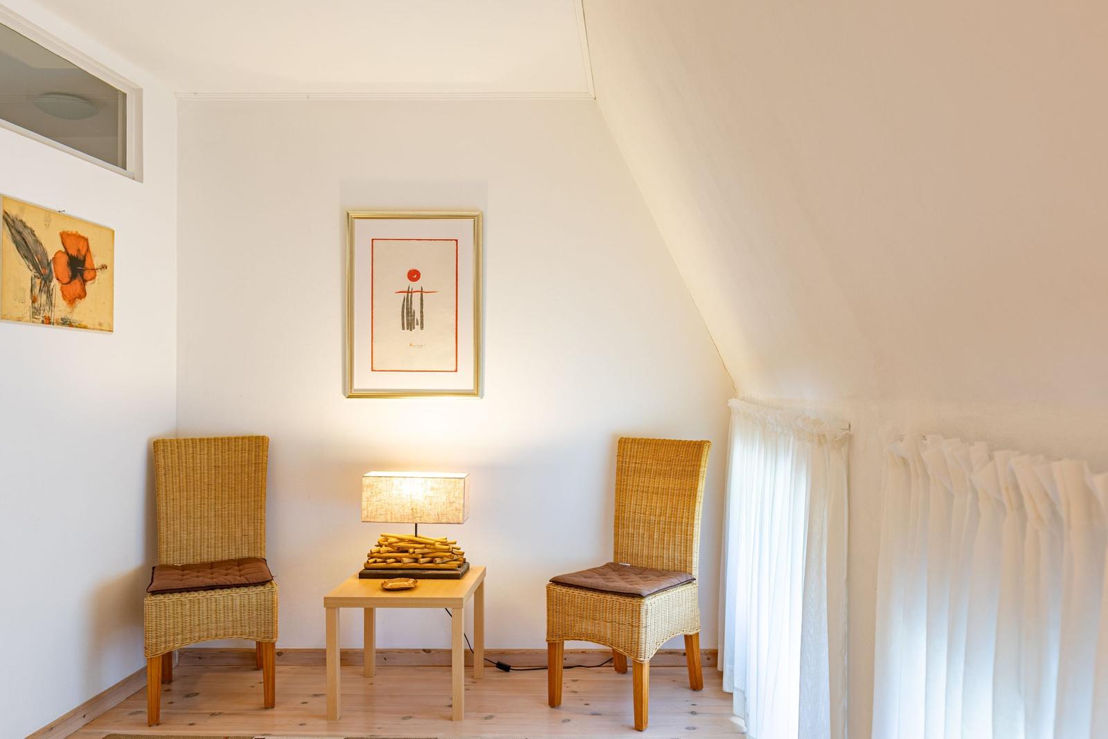Zwei Stühle und ein Tisch mit Lampe unter einem Dachfenster.