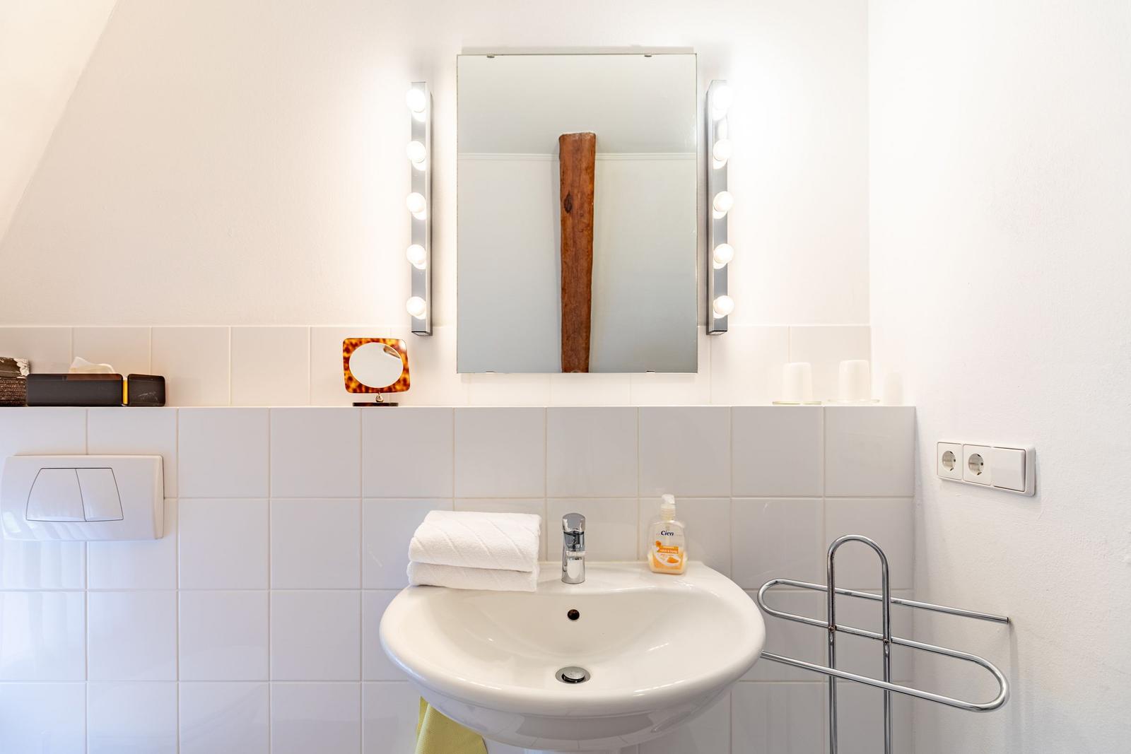 Waschbecken mit Spiegel und Beleuchtung, Handtuch und Seife auf der Arbeitsfläche.