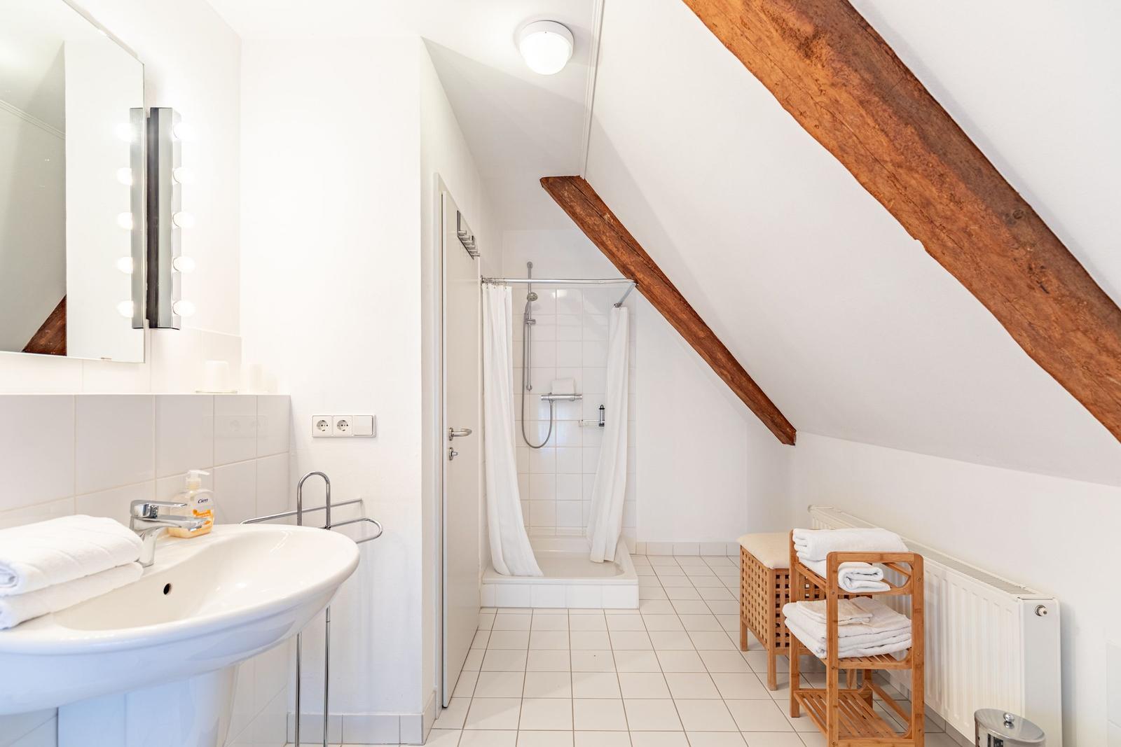 Badezimmer mit Dusche, Waschbecken und Holzbalken an der Decke.