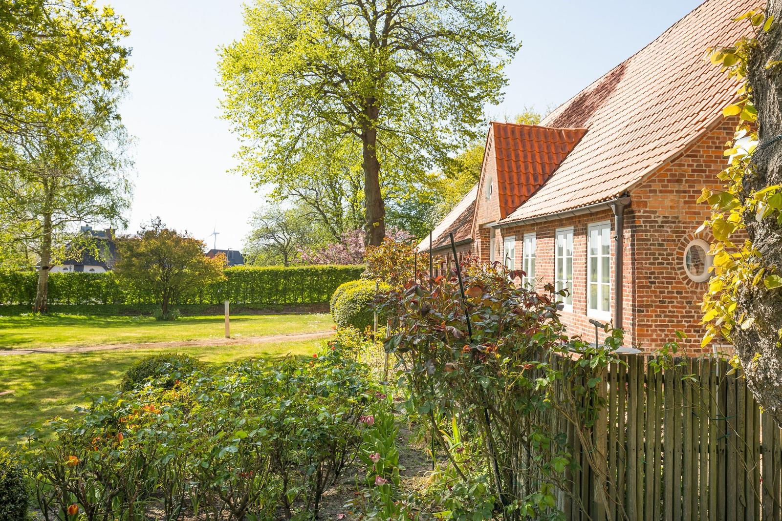 Rotes Ziegeldach, Backsteinhaus mit weißen Fenstern und grünem Garten.