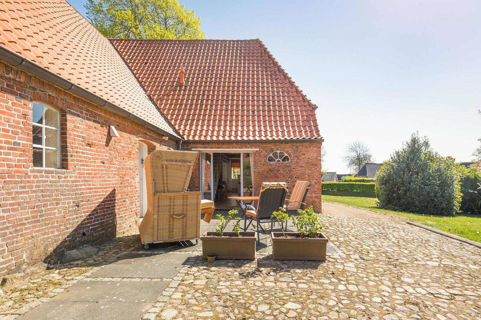 Rotes Ziegeldach, Backsteinhaus mit Terrasse und Garten. Gartenmöbel und Pflanzen auf Kiesweg.
