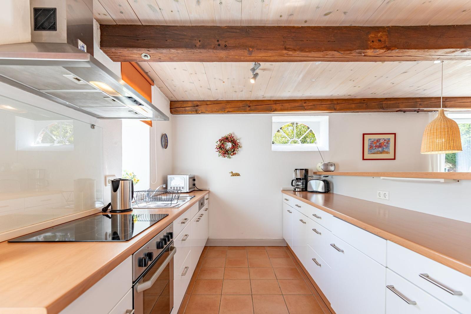 Küche mit Holzdecke, weißen Schränken und Holzplatten. Fenster, Spüle und Kochfeld sichtbar.