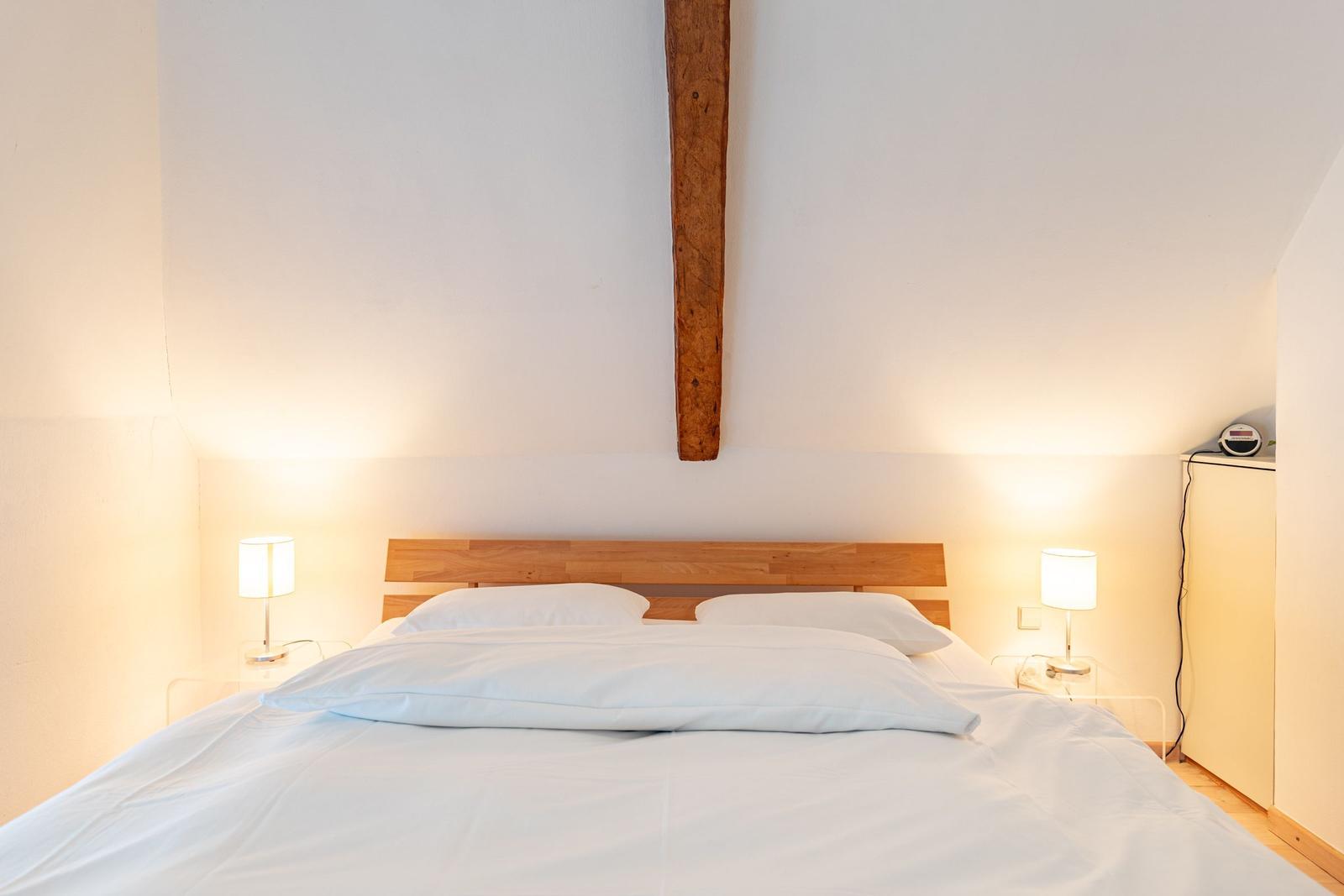 Schlafzimmer mit Bett, zwei Nachttischen und Lampen. Holzständer an der Wand.