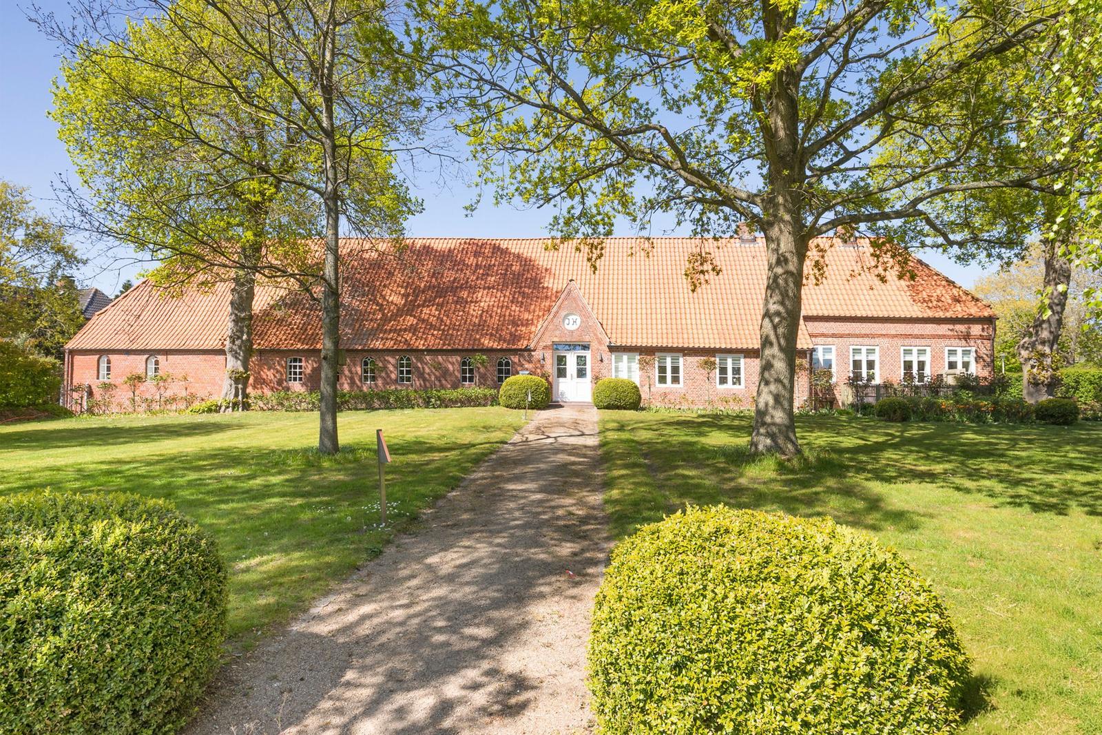 Rotes Backsteingebäude mit Dach und Gartenweg unter Bäumen.