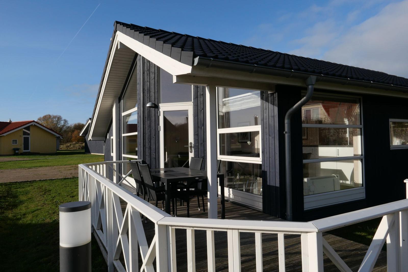 Haus mit Terrasse, Tisch und Stühlen, großflächige Fenster und dunkler Fassade.