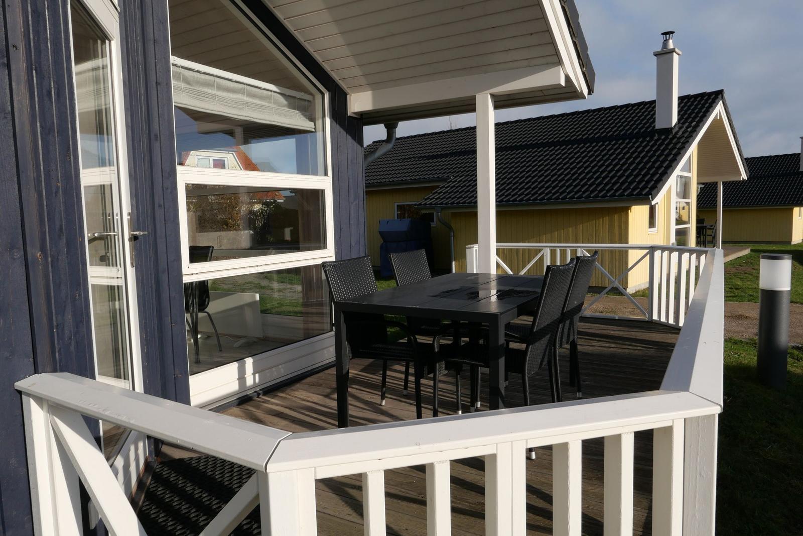 Terrasse mit Tisch und Stühlen vor einem blauen Haus mit weißen Geländern.