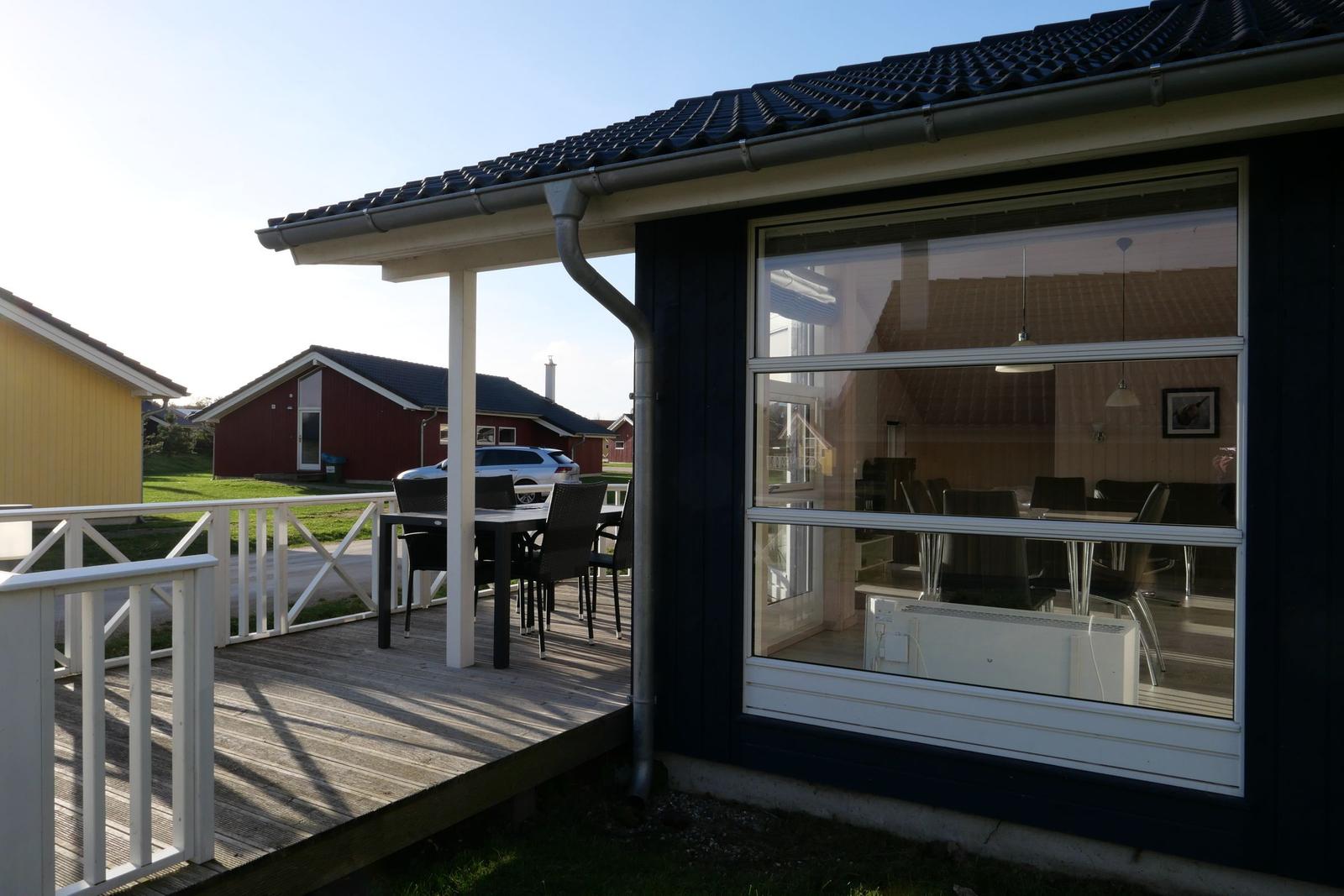 Dunkelblaues Haus mit Terrasse und großer Fensterfront. Im Inneren ist ein Essbereich sichtbar.