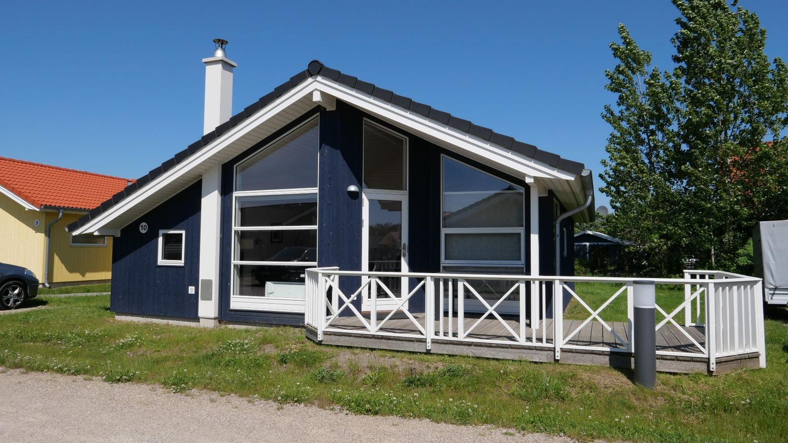 Blau gestrichenes Ferienhaus mit weißem Balkon und großen Fenstern. Hinterhof mit Gras und Bäumen.