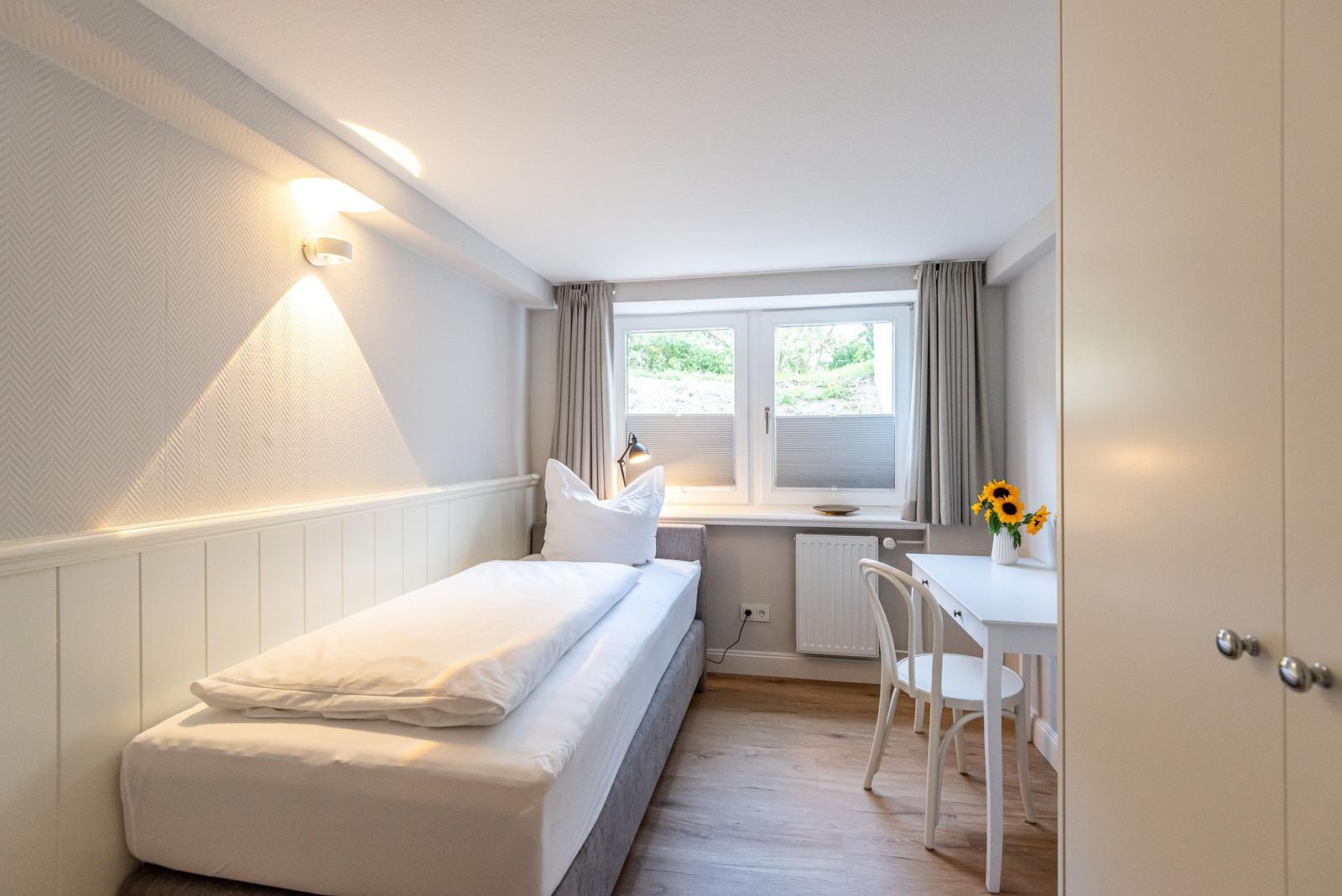 Ein Schlafzimmer mit Bett, Schreibtisch und Fenster mit Blick auf Grün.