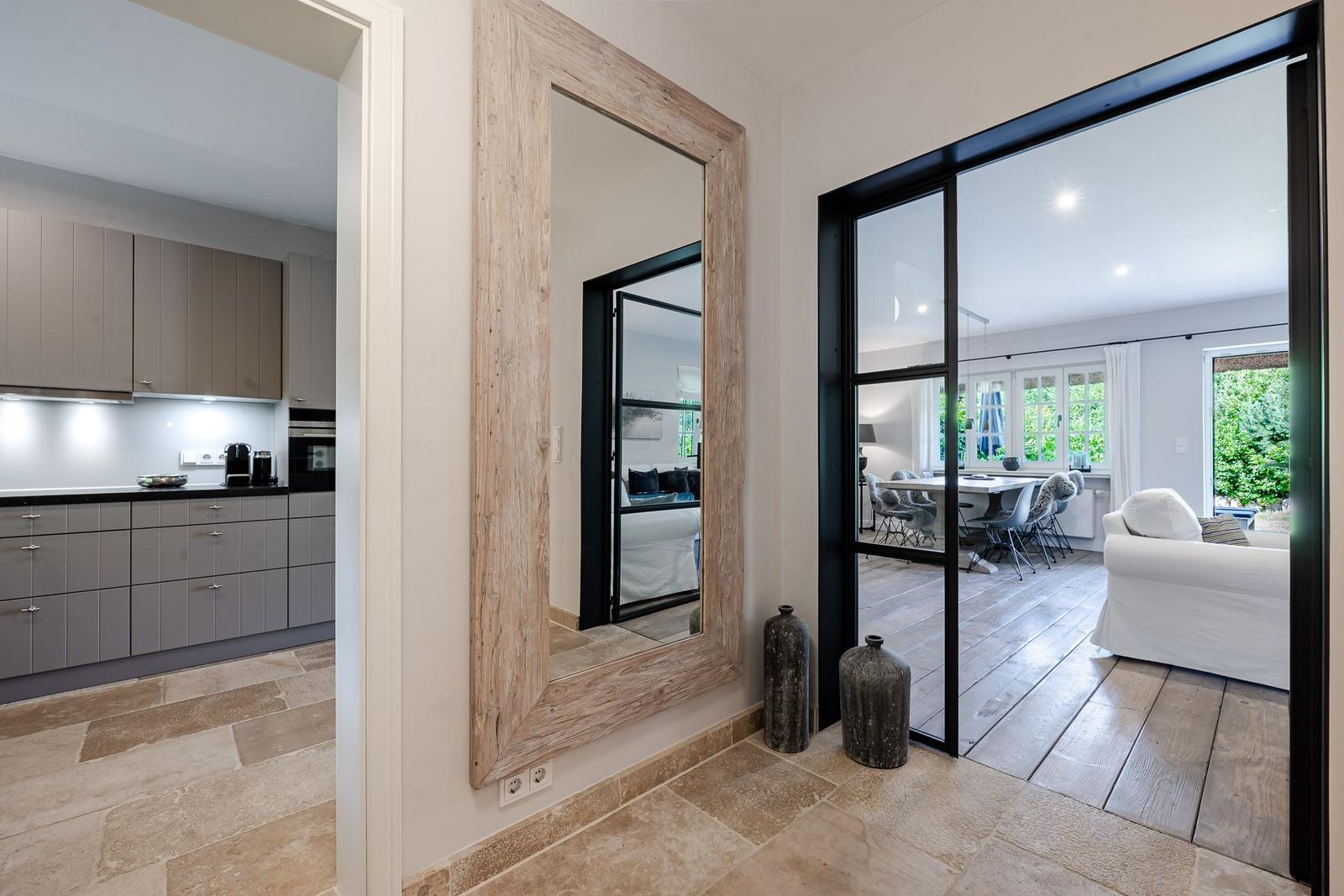 Küche, Wohn- und Essbereich mit Holzboden und Spiegel. Große Fenster mit Blick auf Garten.