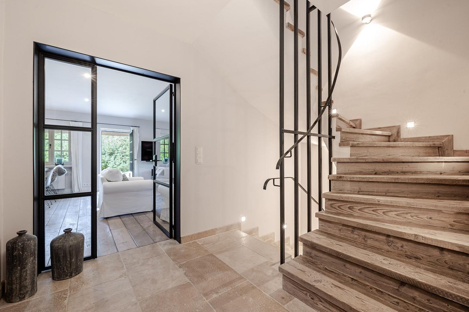 Helle Eingangshalle mit Holztreppe und Glaswand zum Wohnbereich.