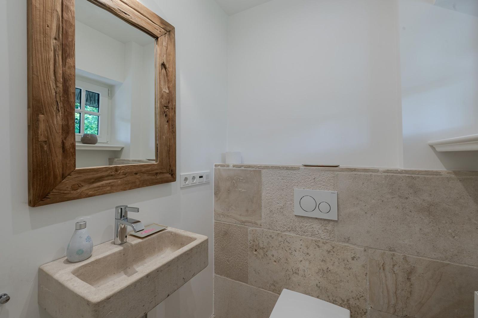 Bad mit Steinwaschbecken, Holzspiegel und Steinwand.