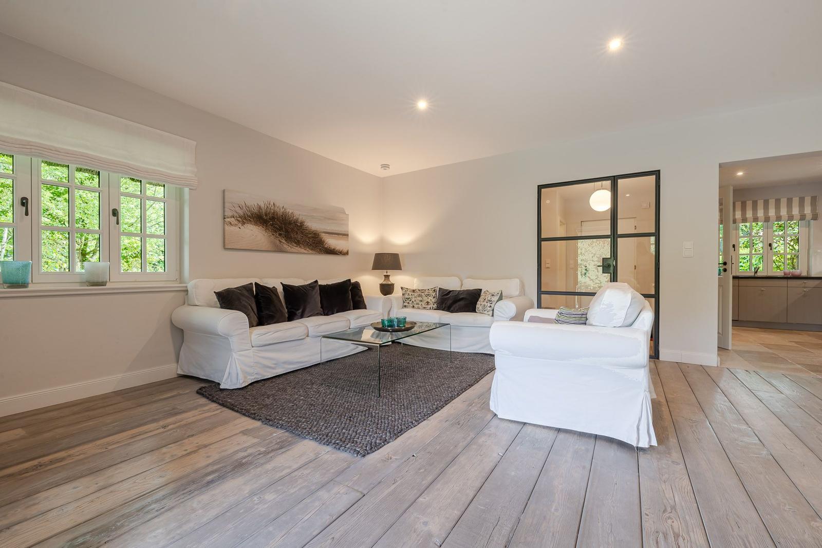 Wohnzimmer mit weißen Sofas, Holzboden und Fenster mit Blick auf Grün.