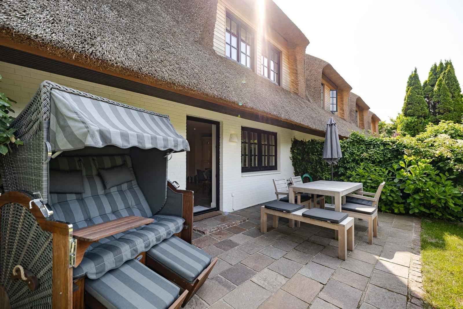 Terrasse mit Strandkorb, Tisch und Stühlen vor einem Haus mit Strohdach.