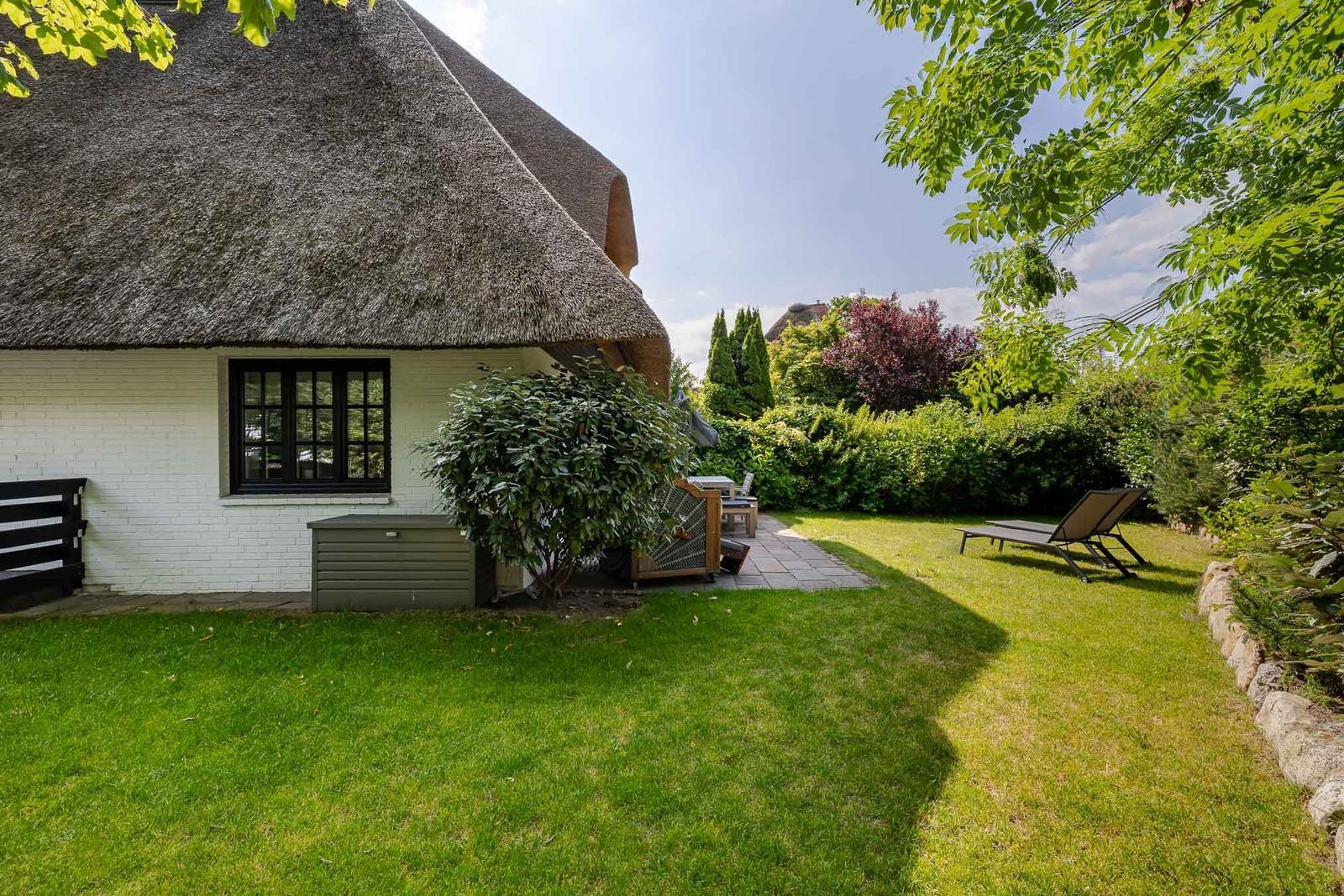 Haus mit Strohdach, Garten mit Liegestühlen und grünem Rasen.