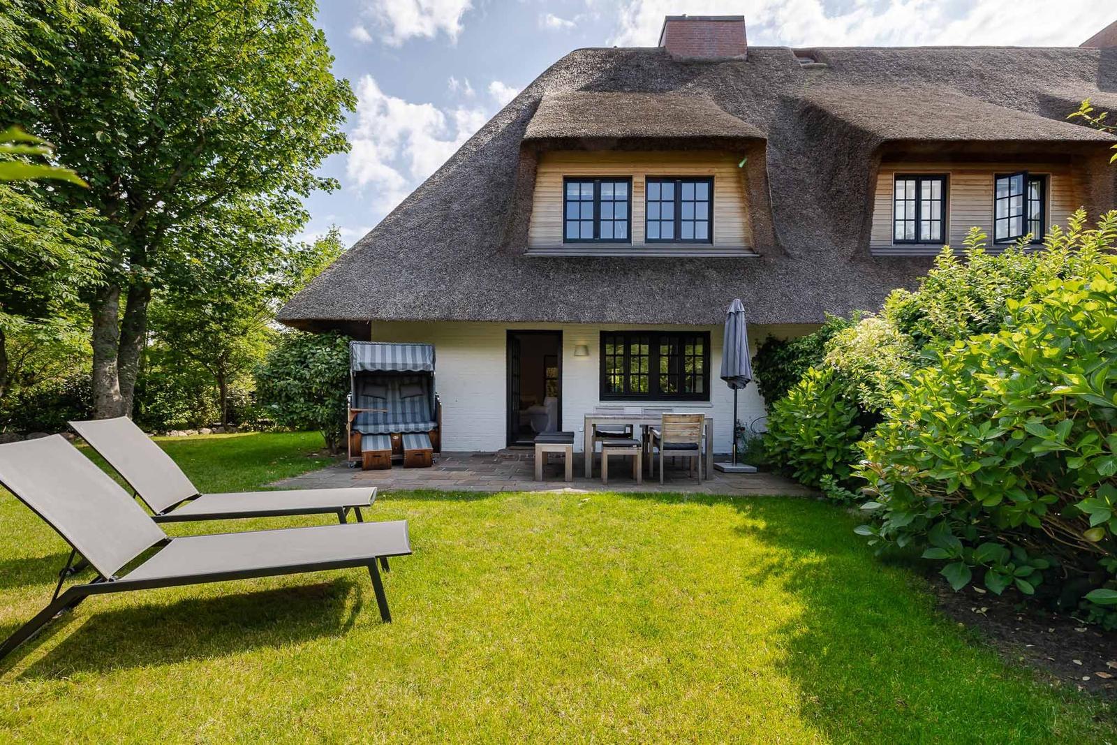 Haus mit Strohdach, Terrasse und Garten mit Liegestühlen.