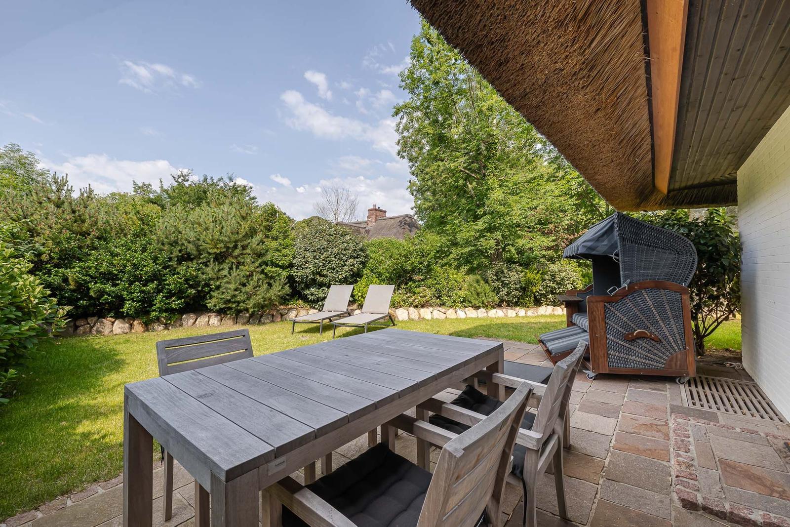 Terrasse mit Tisch, Stühlen und Liegestühlen im Garten unter Dach.