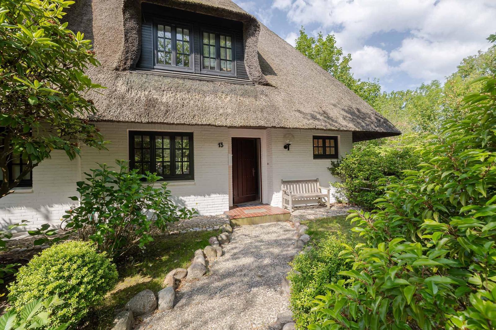 Haus mit Strohdach, weißen Wänden und Gartenweg mit Steinplatten.
