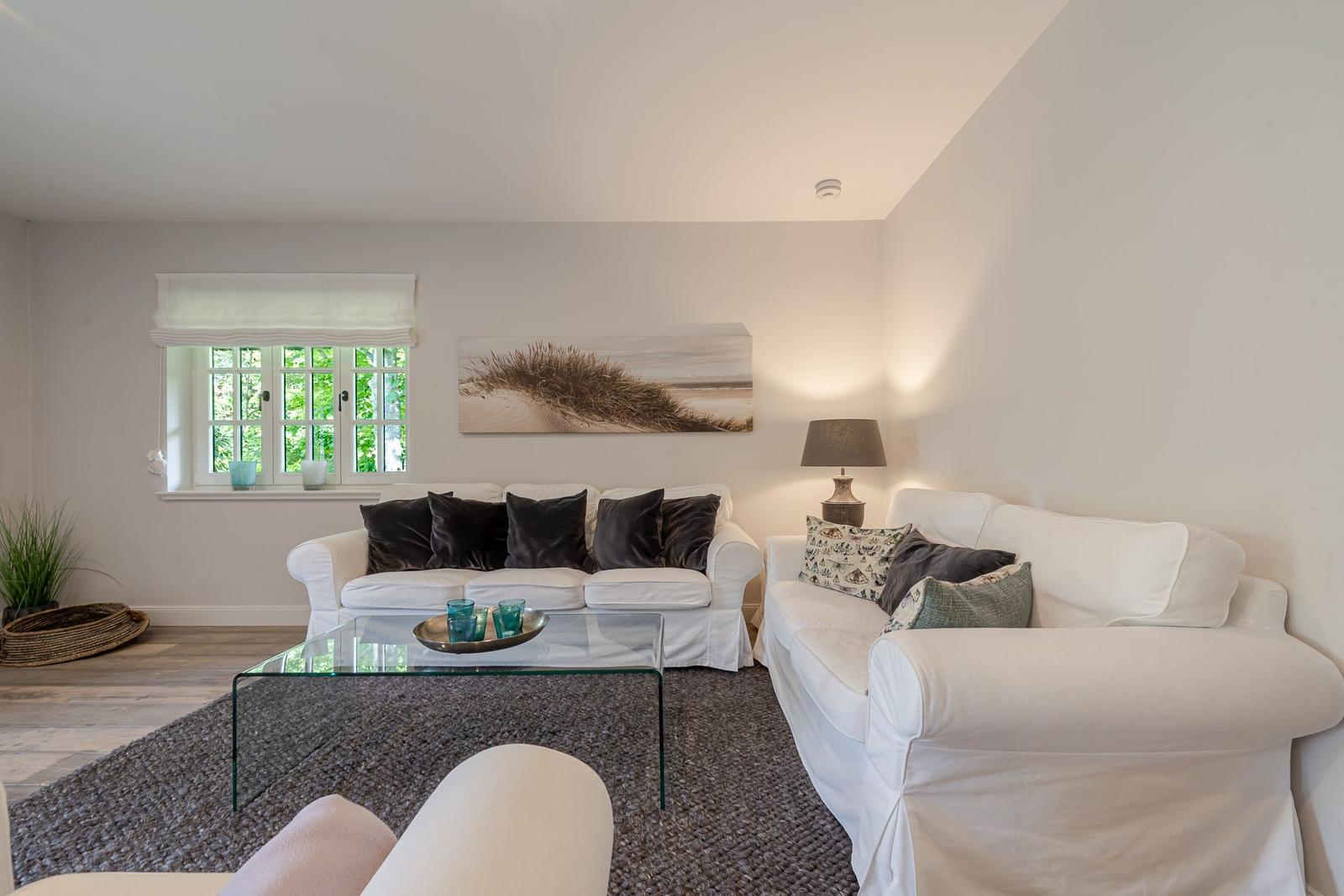 Wohnzimmer mit zwei weißen Sofas, Glas-Tisch und Wandbild.