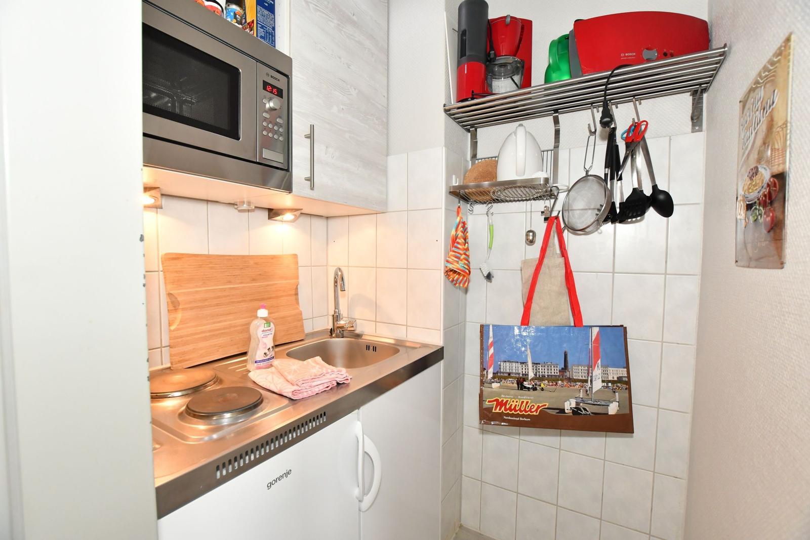 Küche mit Spüle, Herd, Mikrowelle und Küchenutensilien an der Wand.