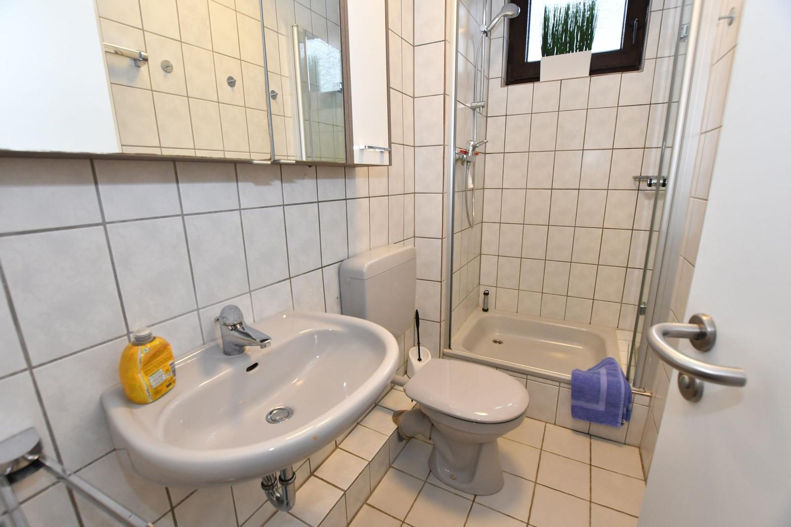 Badezimmer mit Waschbecken, Toilette und Dusche mit Fenster.