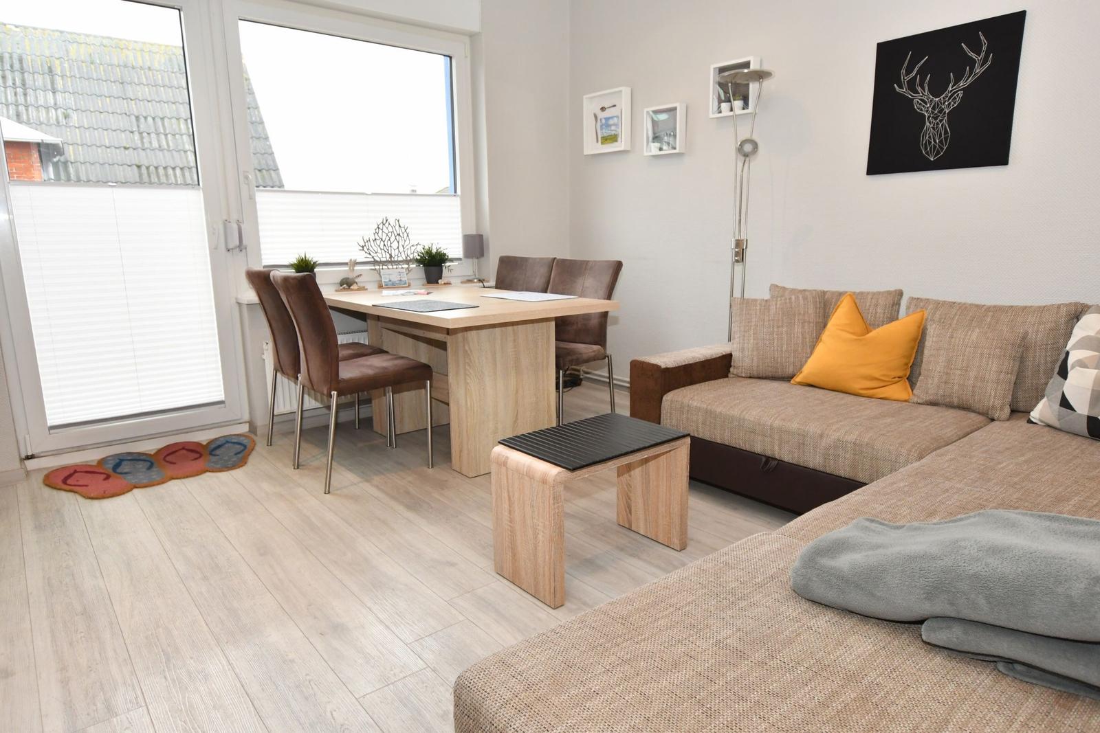 Wohn- und Essbereich mit Sofa, Tisch und Stühlen. Fenster zur Terrasse.