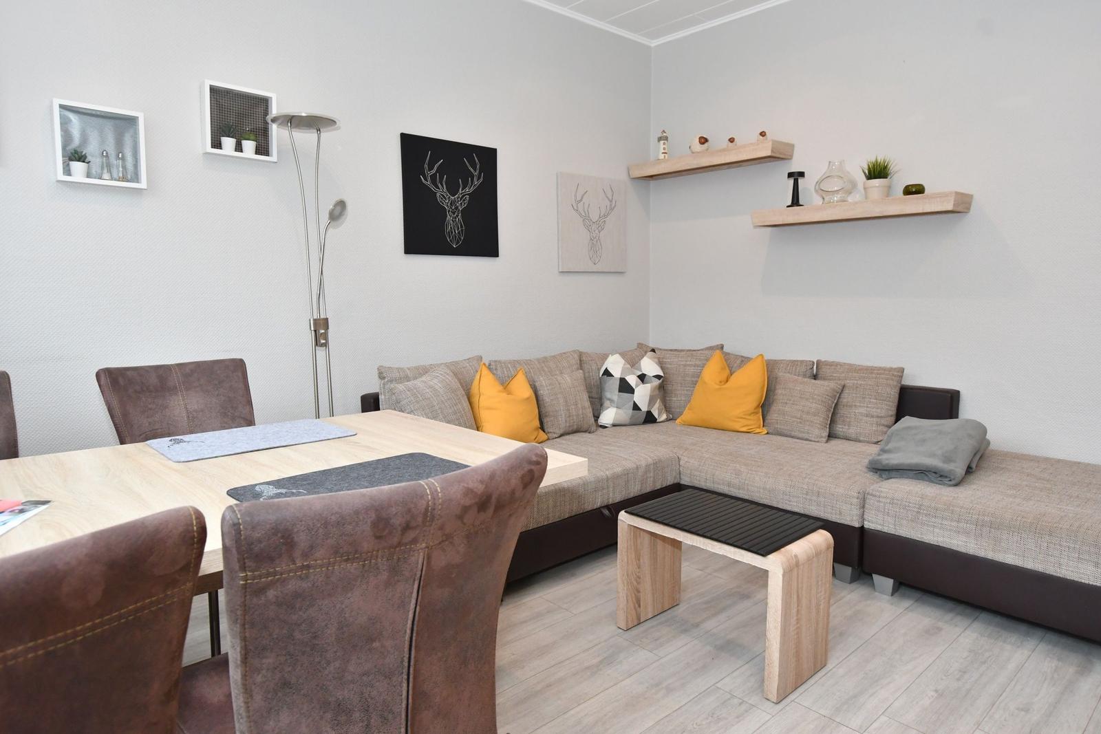 Wohn- und Essbereich mit Ecksofa, Tisch und Stühlen. Wanddekoration und Regale.